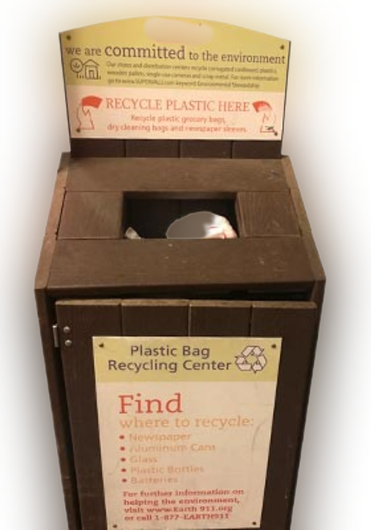 A grocery store drop bin for plastic film made out of brown composite lumber with a  hole for depositing bags and a swing door