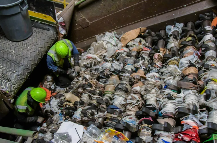 Two workers in safety vets and hard hats cut plastic film from the rollers of a large screen at a recycling facility